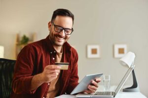 A young couple reviews their finances together at their dining table, paperwork and a laptop open.