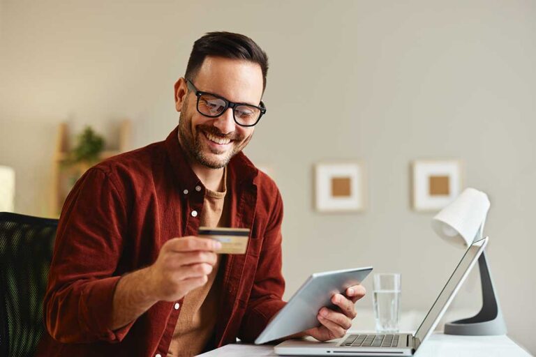 A young couple reviews their finances together at their dining table, paperwork and a laptop open.